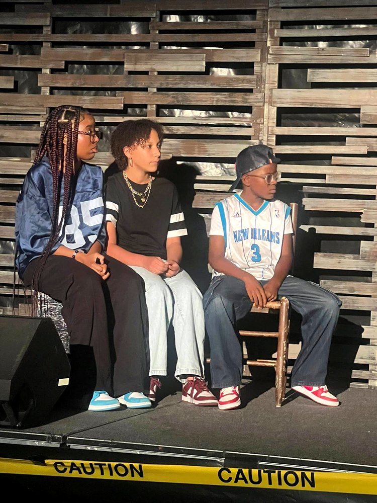 Three young actors seated on stage in front of a wooden slat wall