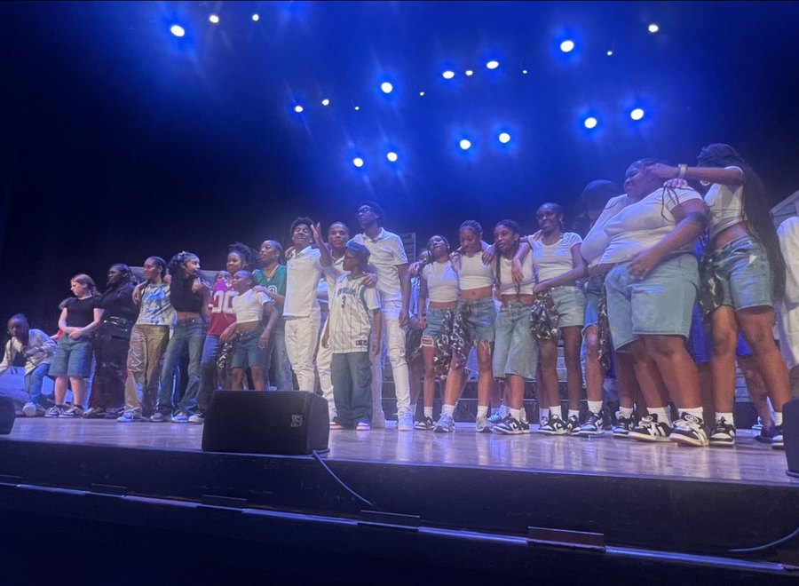The 504 cast linked arm in arm under blue stage lights