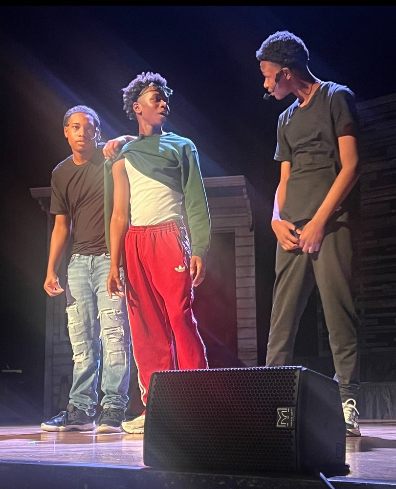 Three young actors in a scene under stage light