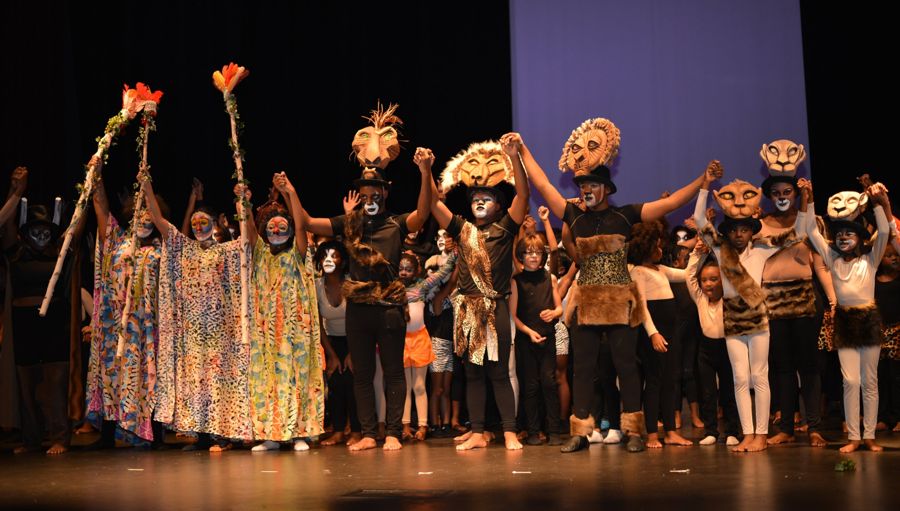 The Lion King youth cast in masks and costumes taking a bow